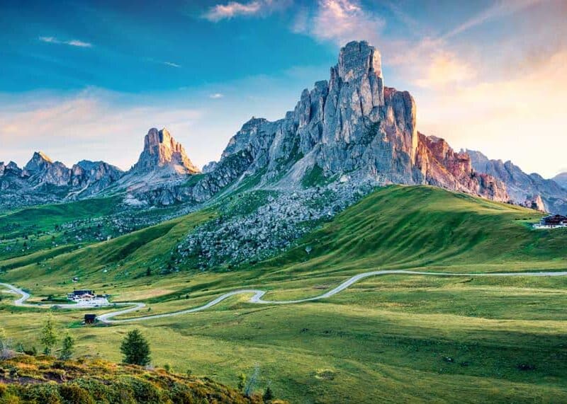 Bergpanorama mit Wolken, Sonne und einer grünen Landschaft im Vordergrund