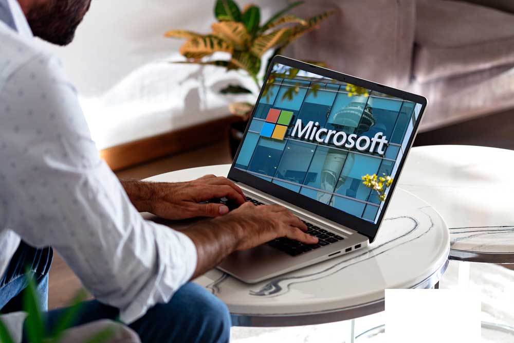 Microsoft Logo auf Laptopdisplay. Davor sitzt ein Mann