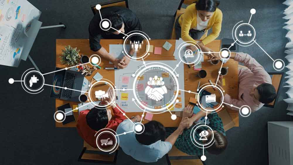 Team arbeitet gemeinsam an digitalen Vertriebsstrategien mit Microsoft Teams und Dynamics 365, symbolisiert durch vernetzte Icons und Zusammenarbeit am Tisch.